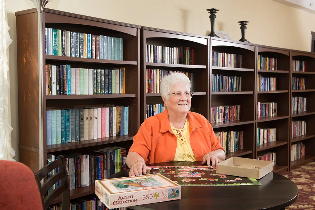 A resident working on a jigsaw puzzle in front of the well-stocked library shelves