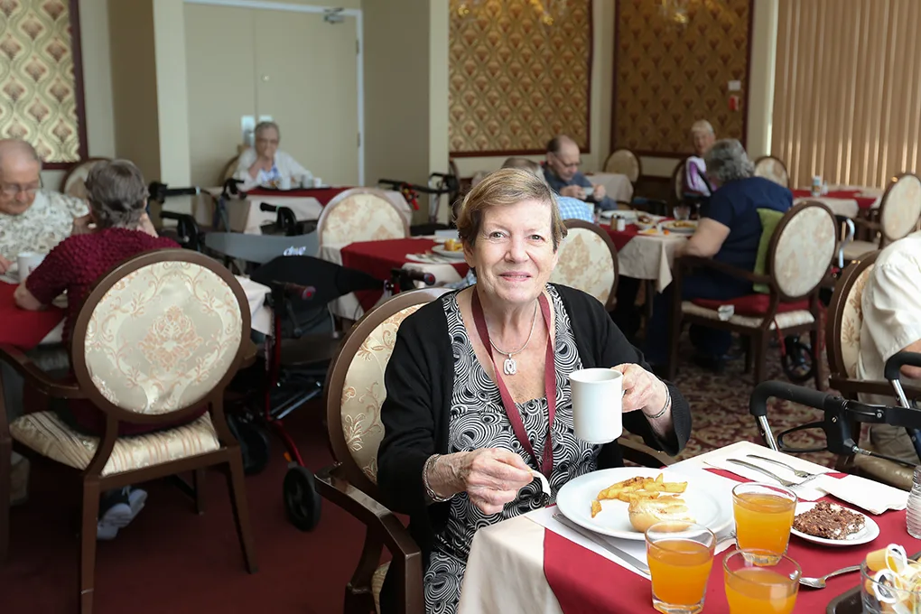 A smiling resident enjoying breakfast in the elegant dining room of Jardins Belle Rive